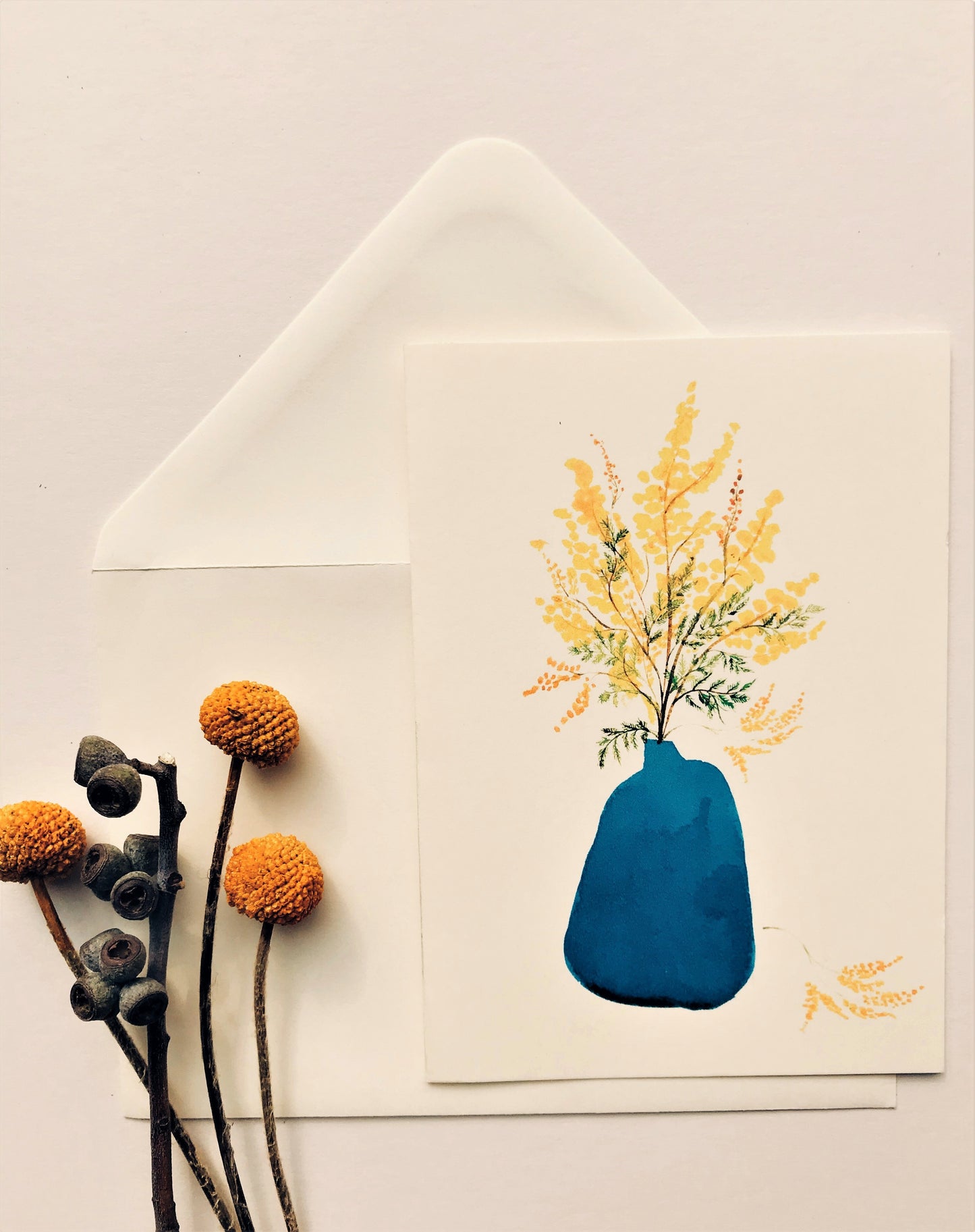 The Blue Vase with Mimosa Greetings Card from Maria Zvaric Illustration features a charming floral design with mimosa blooms arranged in a blue vase. This elegant and versatile card is suitable for various occasions, including birthdays and thank-yous, adding a touch of sophistication and style to your messages.